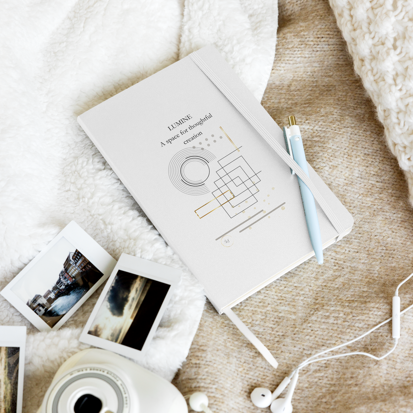 White Lumine hardcover notebook in a lifestyle flat lay with pen, photos and earphones