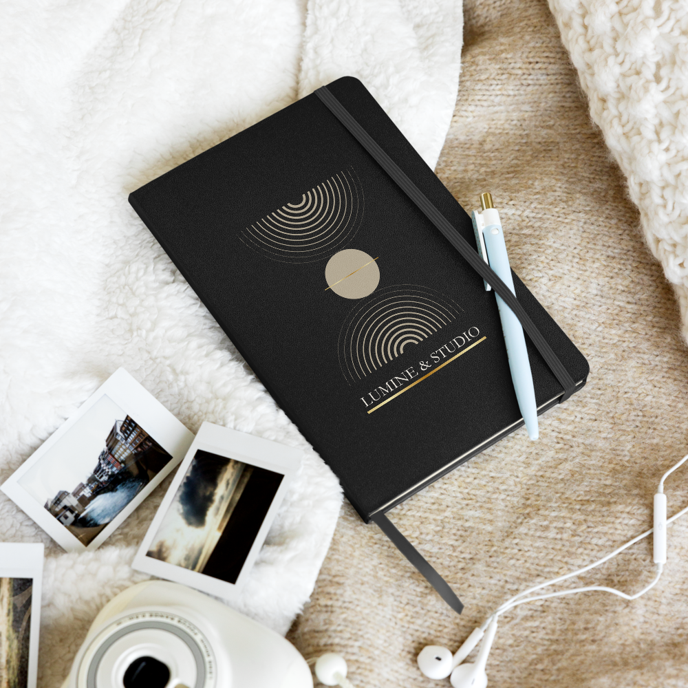 Black Lumine Studio hardcover notebook in a  lifestyle flat lay with pen, photos and earphones