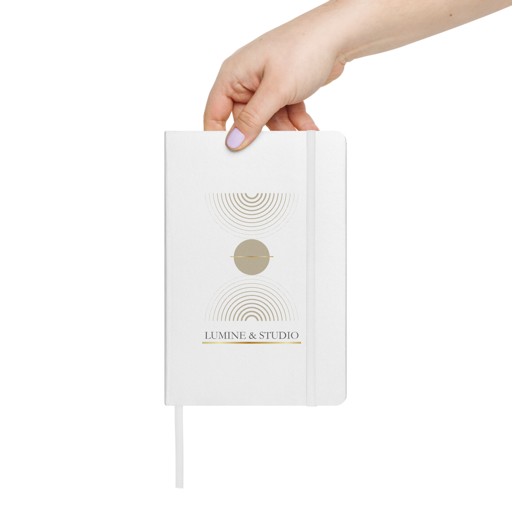 Hand holding the white Lumine Studio hardcover notebook with minimalist gold geometric design