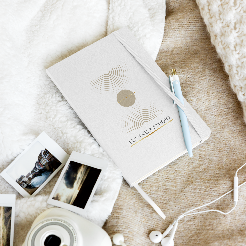 White Lumine Studio hardcover on a lifestyle flat lay with pen, photos and earphones