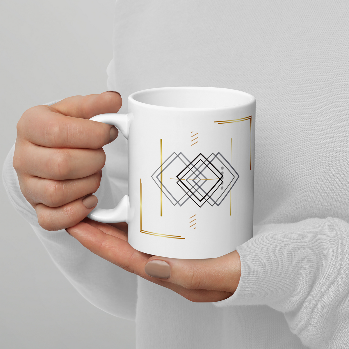 White ceramic mug with minimalist geometric line art and subtle gold detils, held in both hands.