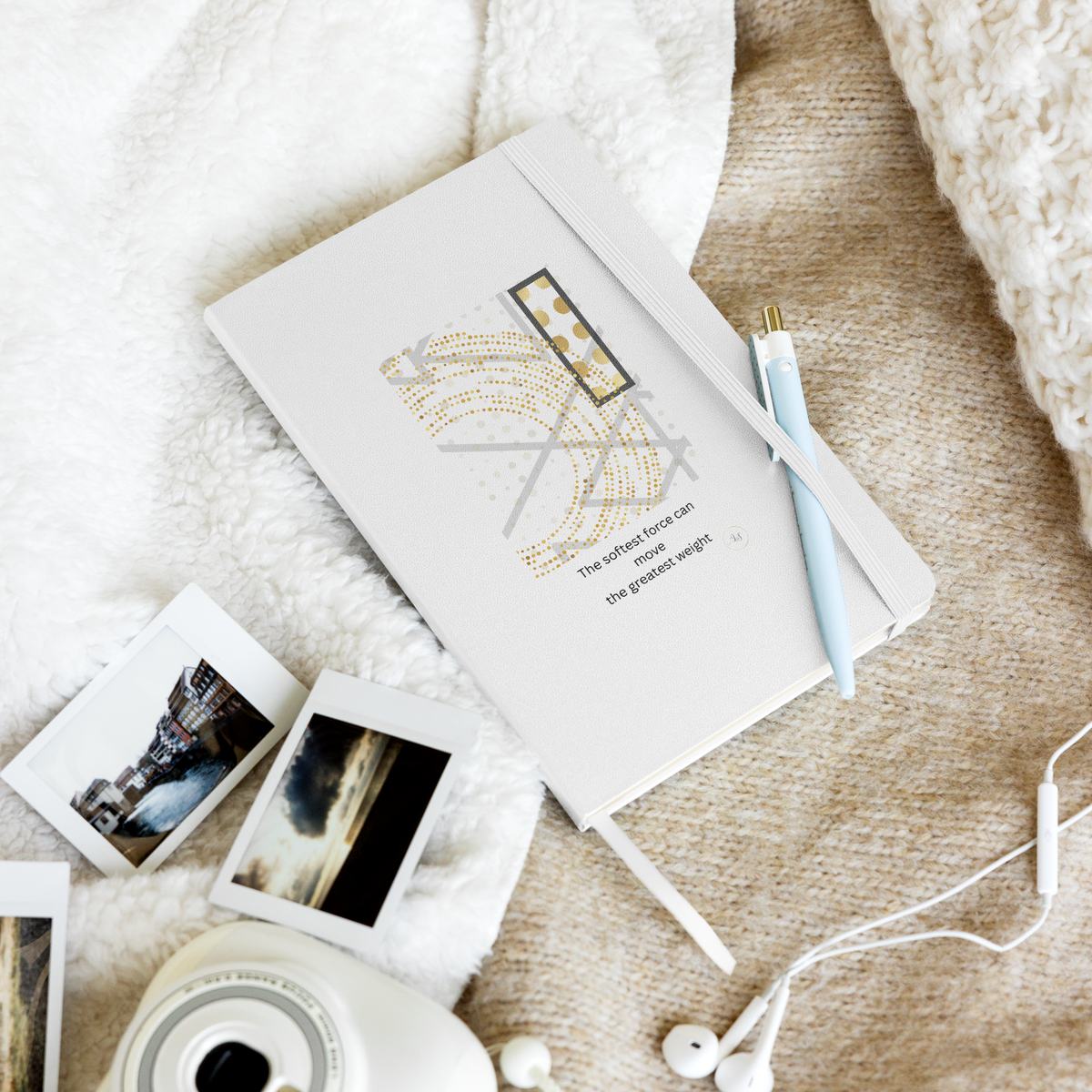 White hardcover notebook with minimalist geometric line art and subtle gold details styled with a pen, photos and earphones on a soft textured surface.